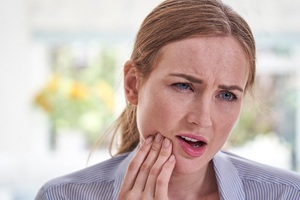 Woman with failed dental implants in Plano, TX rubbing jaw in pain