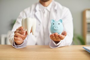 Dentist holding tooth model and piggy bank