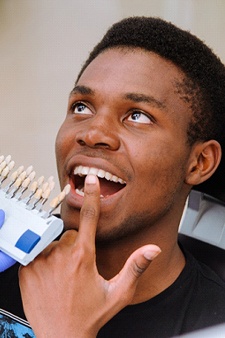 A male patient points to a tooth while the dentist uses a shade guide to determine the appropriate color