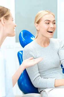 A young female patient looking at her smile in the mirror while the dentist sits nearby