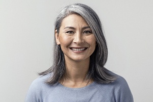 A middle-aged woman wearing a blue sweater and smiling, showing off her recent cosmetic bonding in Plano treatment