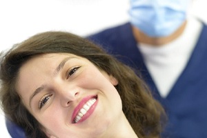 A young woman with dark hair lying back in a dentist’s chair and showing off her smile