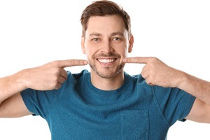 A young man wearing a blue shirt and pointing to his smile after having cosmetic bonding treatment