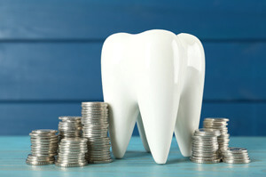 a large ceramic tooth model next to stacks of silver coins