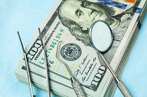 dental instruments lying on top of a stack of hundred-dollar bills