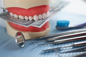 A jaw mockup biting money while sitting next to dental instruments on a table