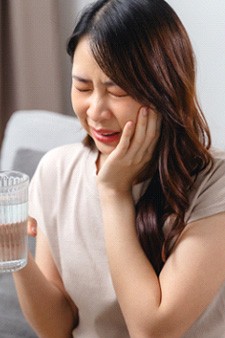a woman experiencing dental sensitivity after drinking water holding her mouth in pain