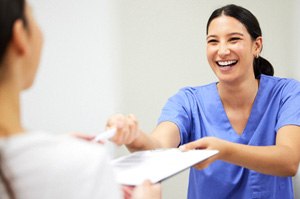 a front desk staff member handing a patient forms on a clipboard 