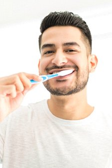 a smiling man brushing his teeth