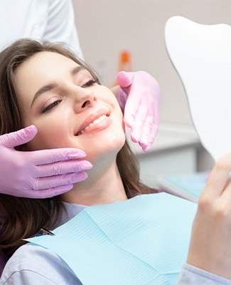 Woman in dental chair admiring reflection in tooth-shaped mirror
