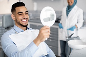 Man smiling while looking at reflection in handheld mirror