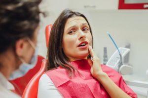 Woman in dental chair clutching aching jaw 