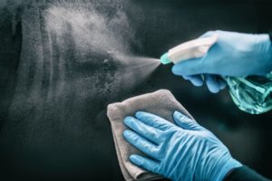 person sanitizing a surface with gloves on 